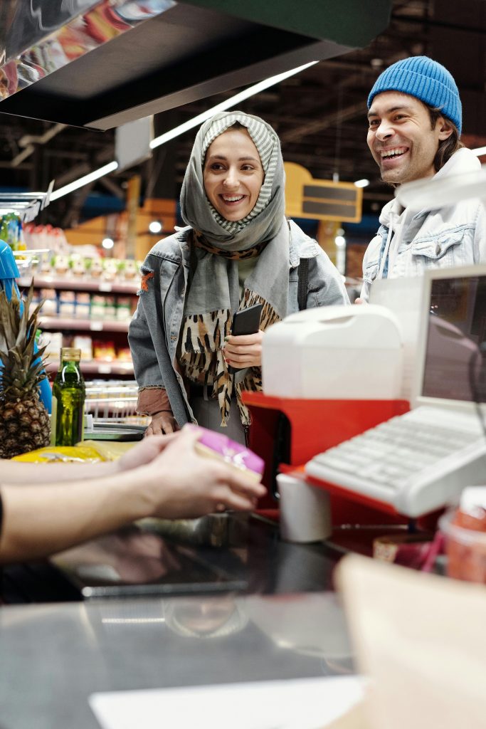 A smiling couple at a supermarket checkout counter, engaging in a cheerful shopping experience.